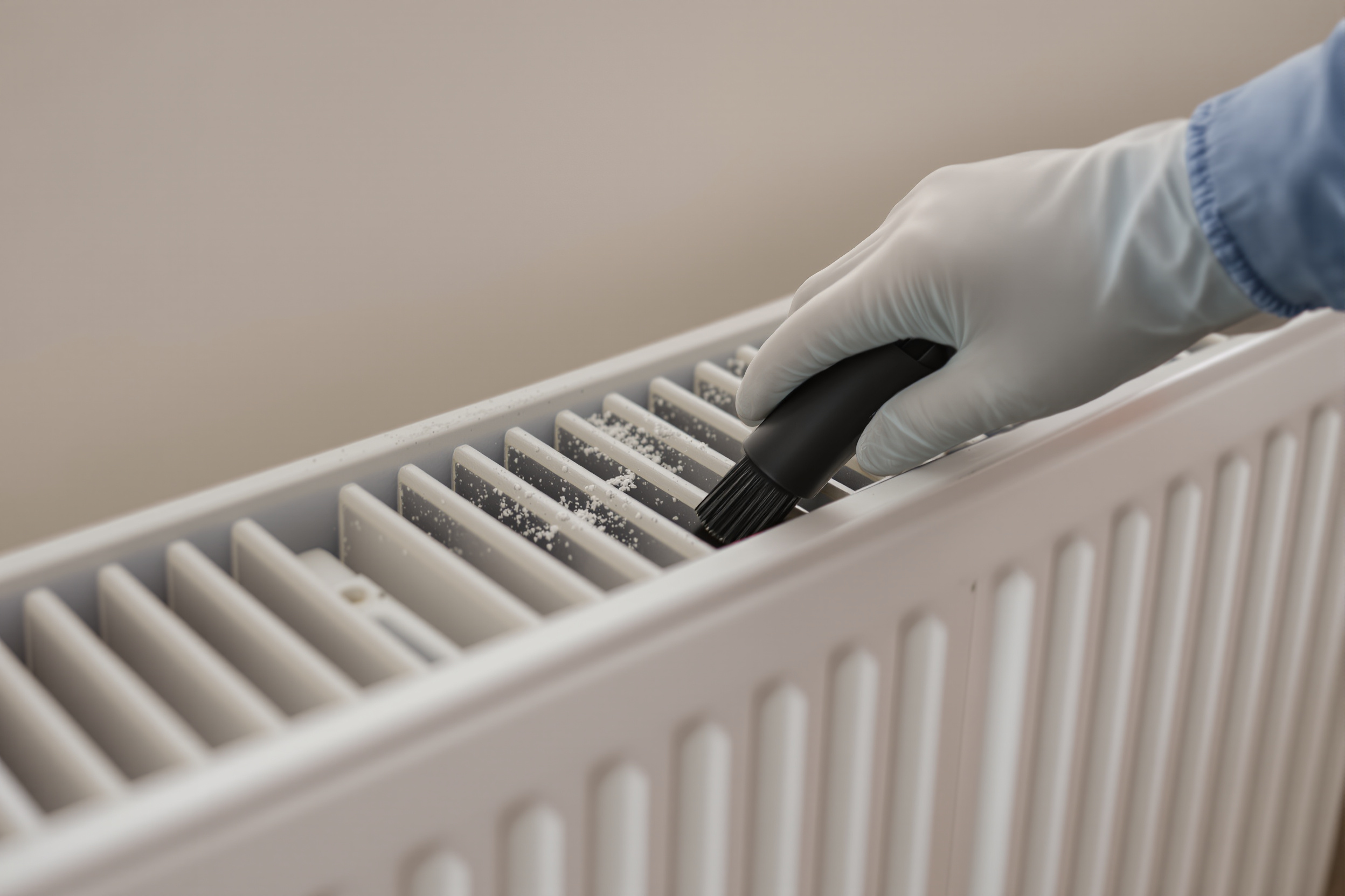 Brush nozzle of a HEPA vacuum removing plaster dust from between the fins of a panel radiator after building work